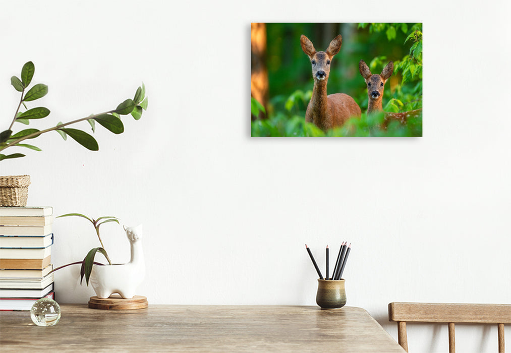 Premium Textil-Leinwand Eine Rehgeiß steht mit ihrem Kitz im grünen Frühlingswald und blickt aufmerksam durch das frische Laub.
